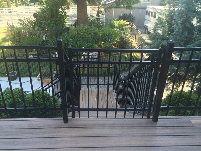 Black metal gate and railing on deck overlooking steps, with greenery in the background.