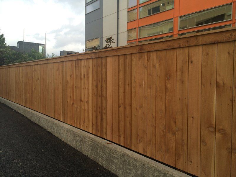 Wooden fence along a concrete curb, with a multi-story building in the background.