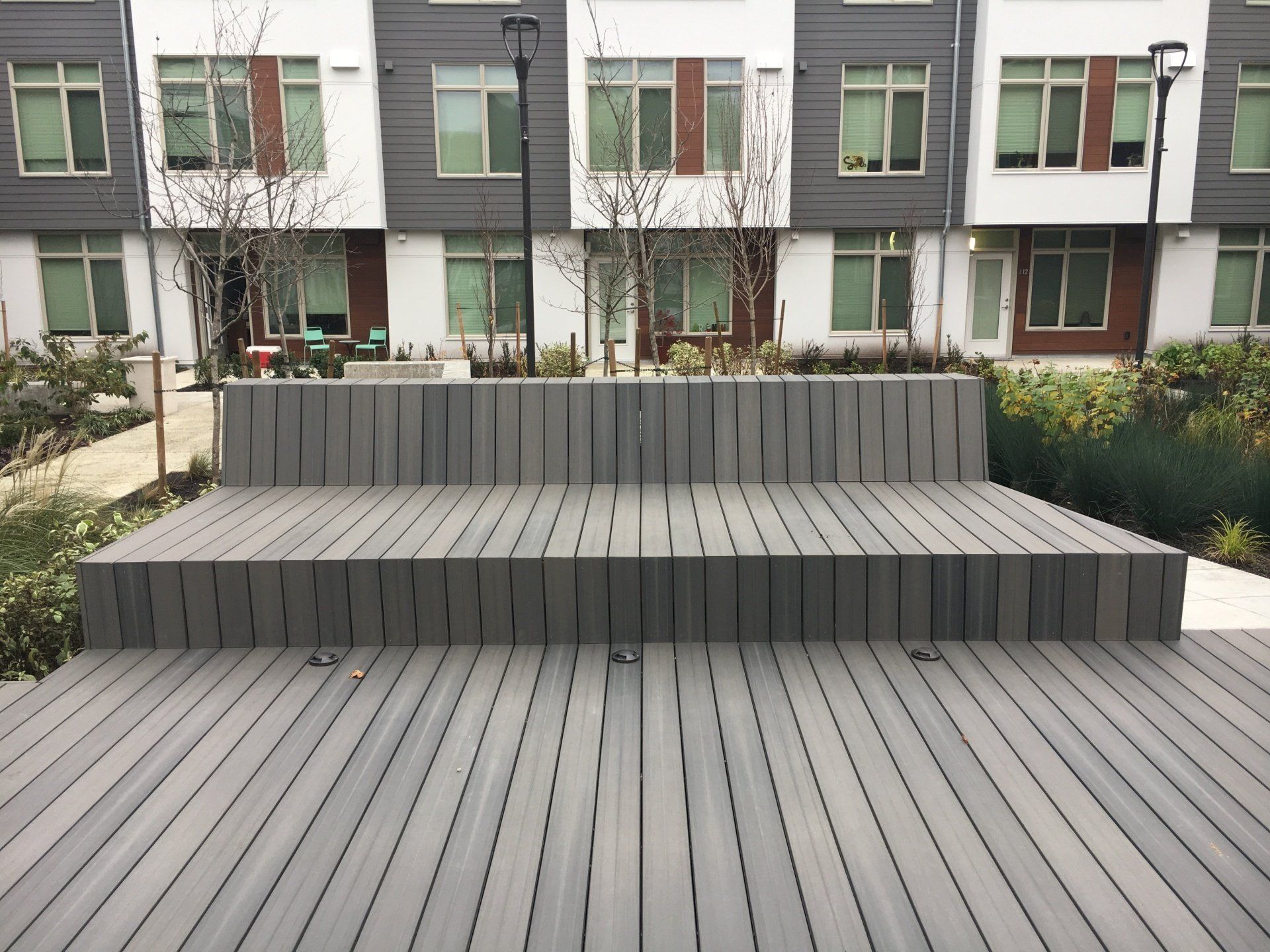Gray tiered wooden bench in front of a modern building with windows.