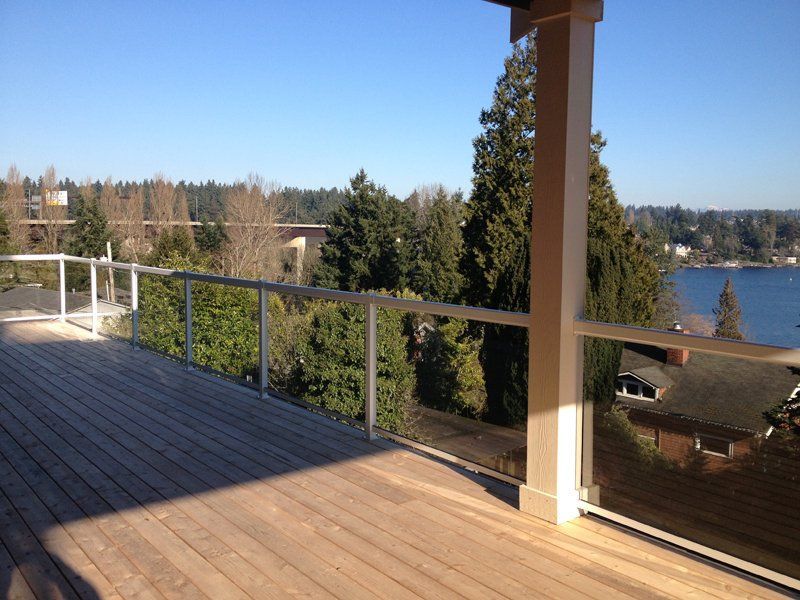 Wooden deck with glass railing overlooking a body of water and trees on a sunny day.
