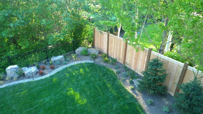 Green lawn with landscaped border, wooden fence, and trees.