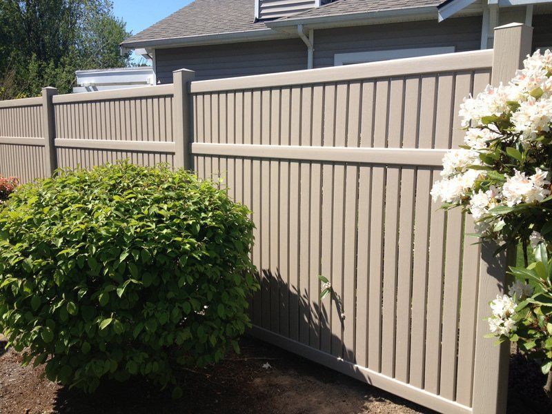 Beige vertical-slat fence bordering a yard with green shrubs and a white flowering bush.