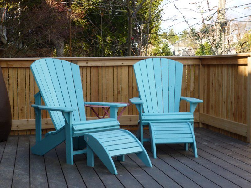 Two light blue Adirondack chairs and a footrest on a wooden deck, with a wooden fence in the background.