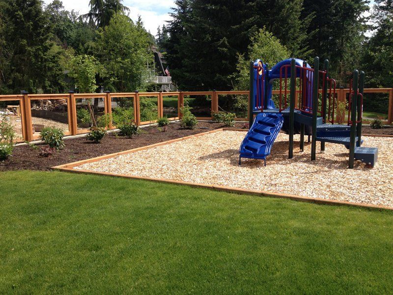 Playground with blue slide, wood fence, and wood chip ground cover.