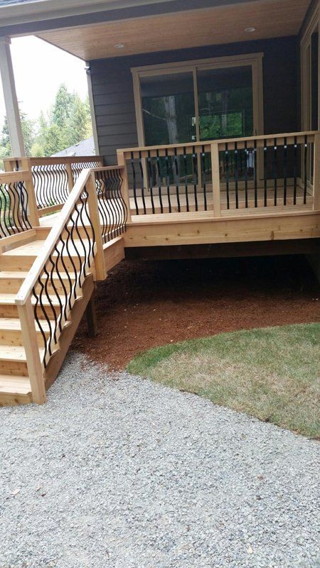 Wooden deck with stairs, black iron railings, and sliding glass door. Mulch and gravel ground cover.