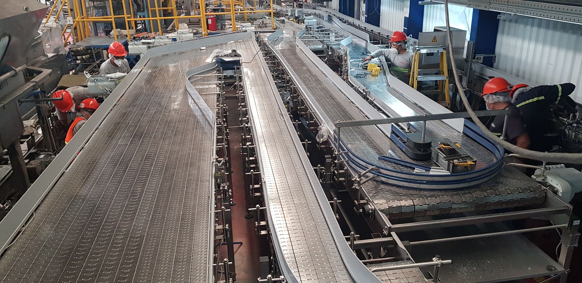 Sistema de cinta transportadora industrial en una fábrica, con trabajadores inspeccionando la maquinaria a lo largo.