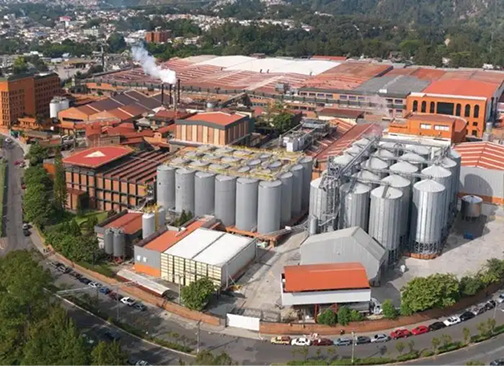 Vista aérea de una instalación industrial con grandes tanques plateados, edificios con techos rojos.