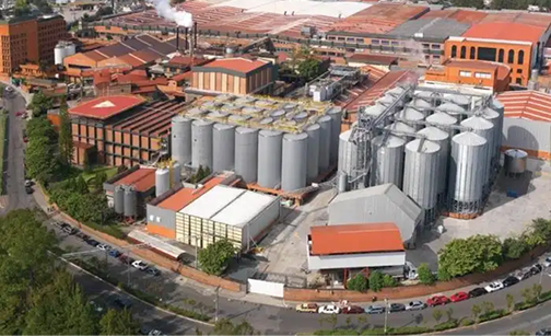 Vista aérea de una planta industrial con grandes tanques de almacenamiento plateados y edificios con techos rojos.