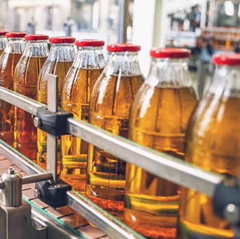 Botellas de vidrio con tapones rojos llenas de líquido ámbar se desplazan a lo largo de una cinta transportadora.