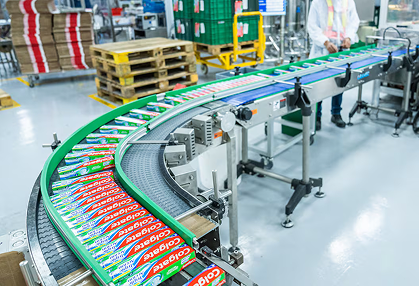 Una cinta transportadora curva mueve productos empaquetados de colores a través de un piso de fábrica limpio.