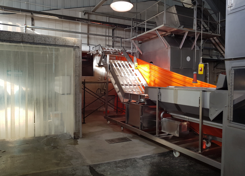 Máquina industrial procesando material de color naranja brillante en una cinta transportadora en un entorno de fábrica.
