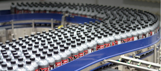 Filas de latas de bebidas plateadas moviéndose a lo largo de una cinta transportadora azul curva en una fábrica.
