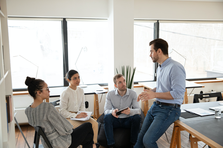A group of people are sitting around a table in an office having a meeting.