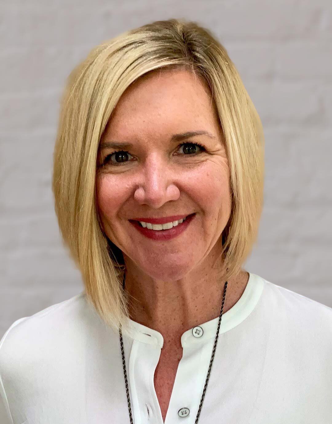 A woman with blonde hair and a white shirt is smiling for the camera.