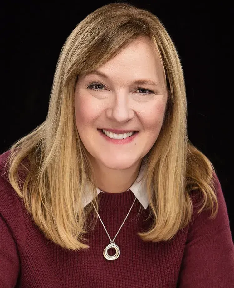 A woman wearing a red sweater and a necklace is smiling.