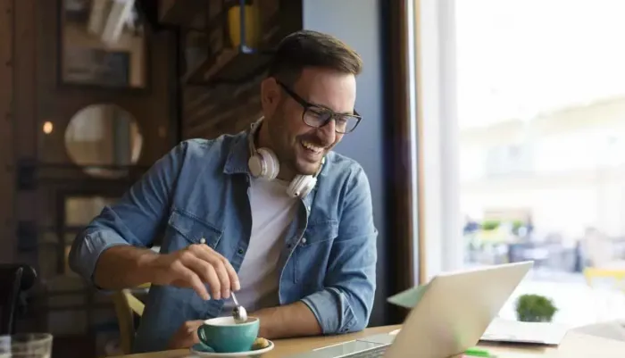 A man is sitting at a table with a cup of coffee and a laptop.