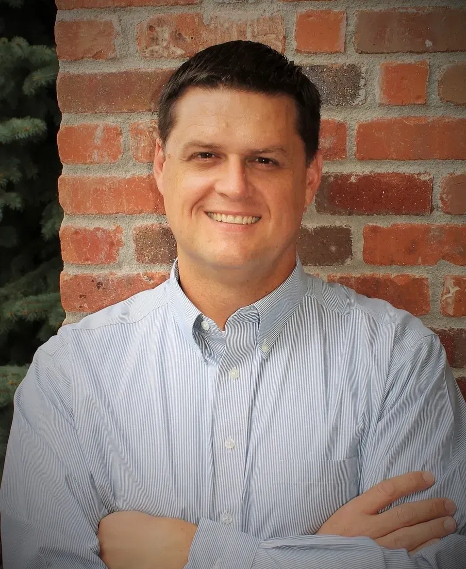 A man with his arms crossed is smiling in front of a brick wall
