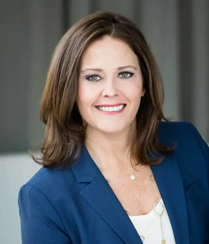 A woman in a blue jacket and white shirt is smiling for the camera.
