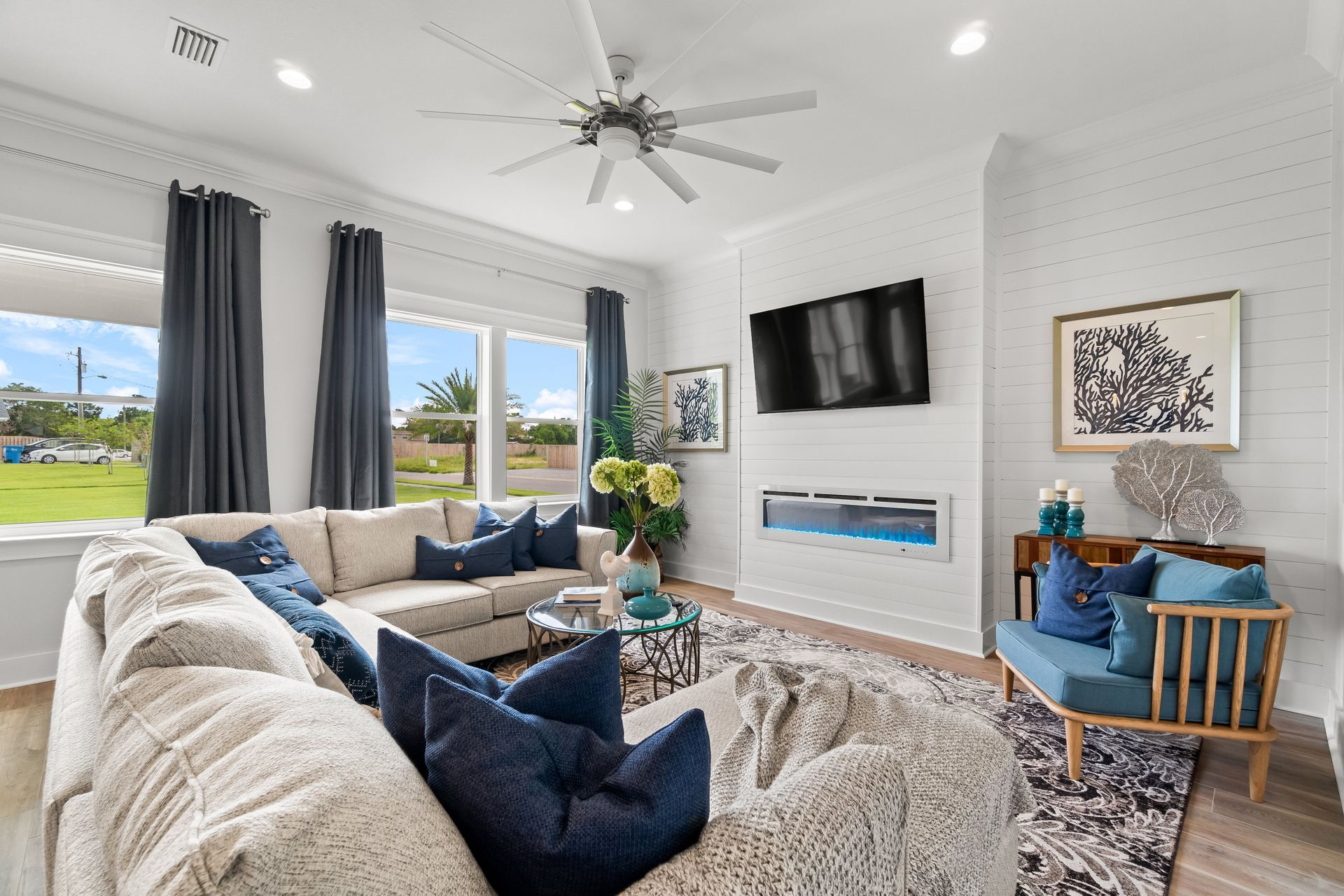 Living room with a large sectional sofa, fireplace, TV, and large windows with blue curtains.