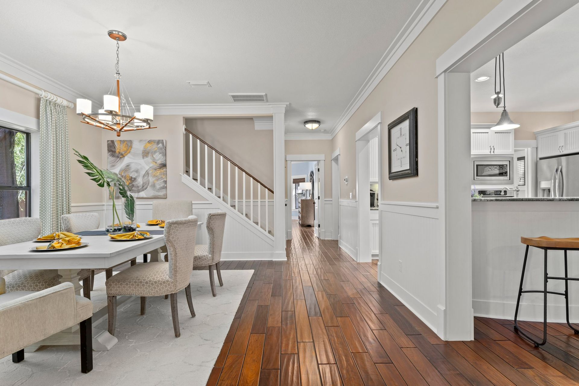 Dining room with white table, chairs, hardwood floors, and staircase.