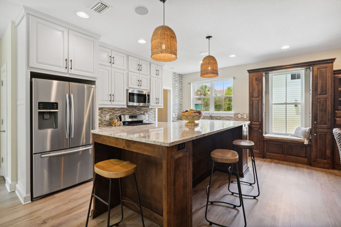 Kitchen with white cabinets, stainless steel refrigerator, island with stools, and woven pendant lights.