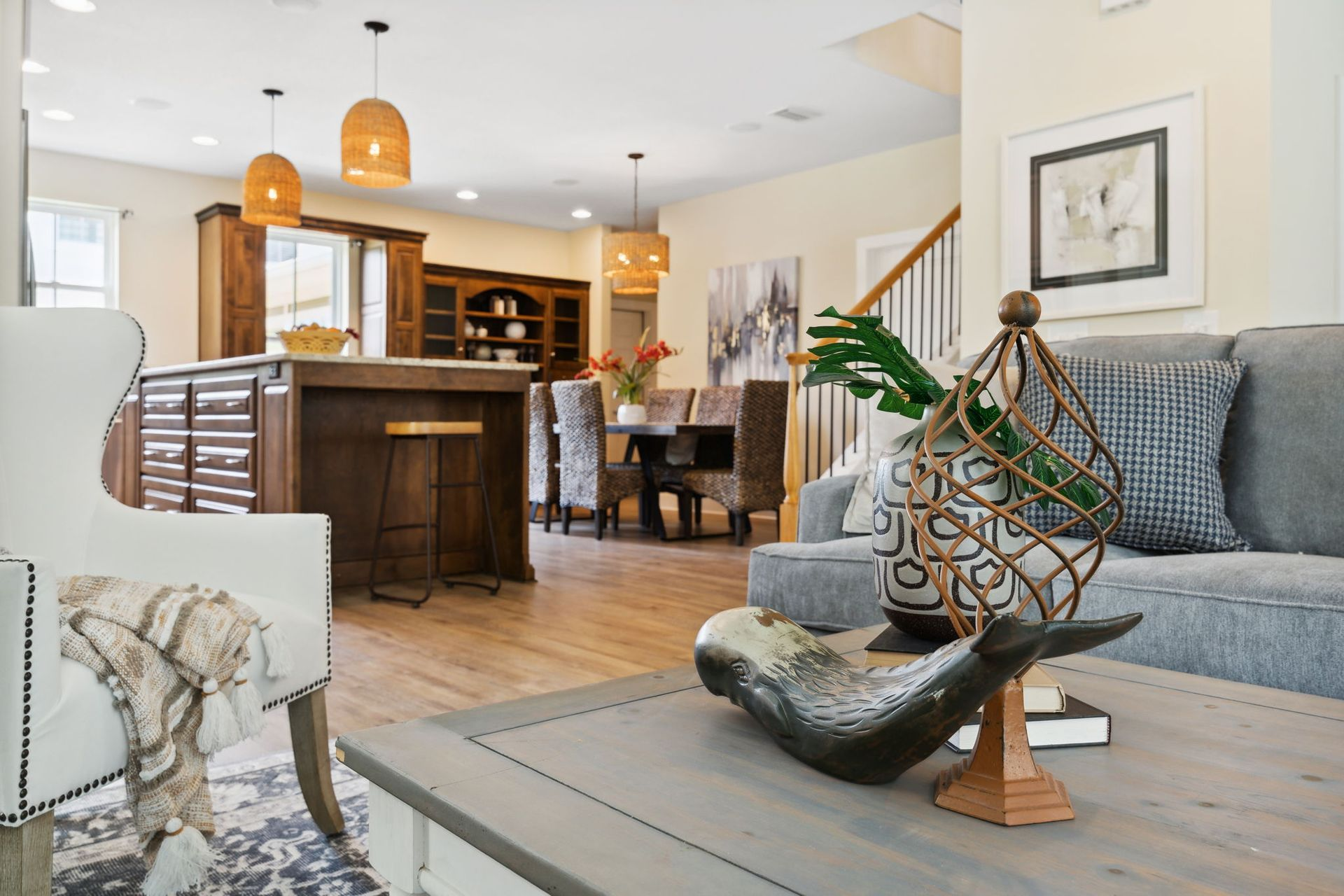 Open-concept living room and kitchen with gray sofa, wood bar stools, and pendant lights