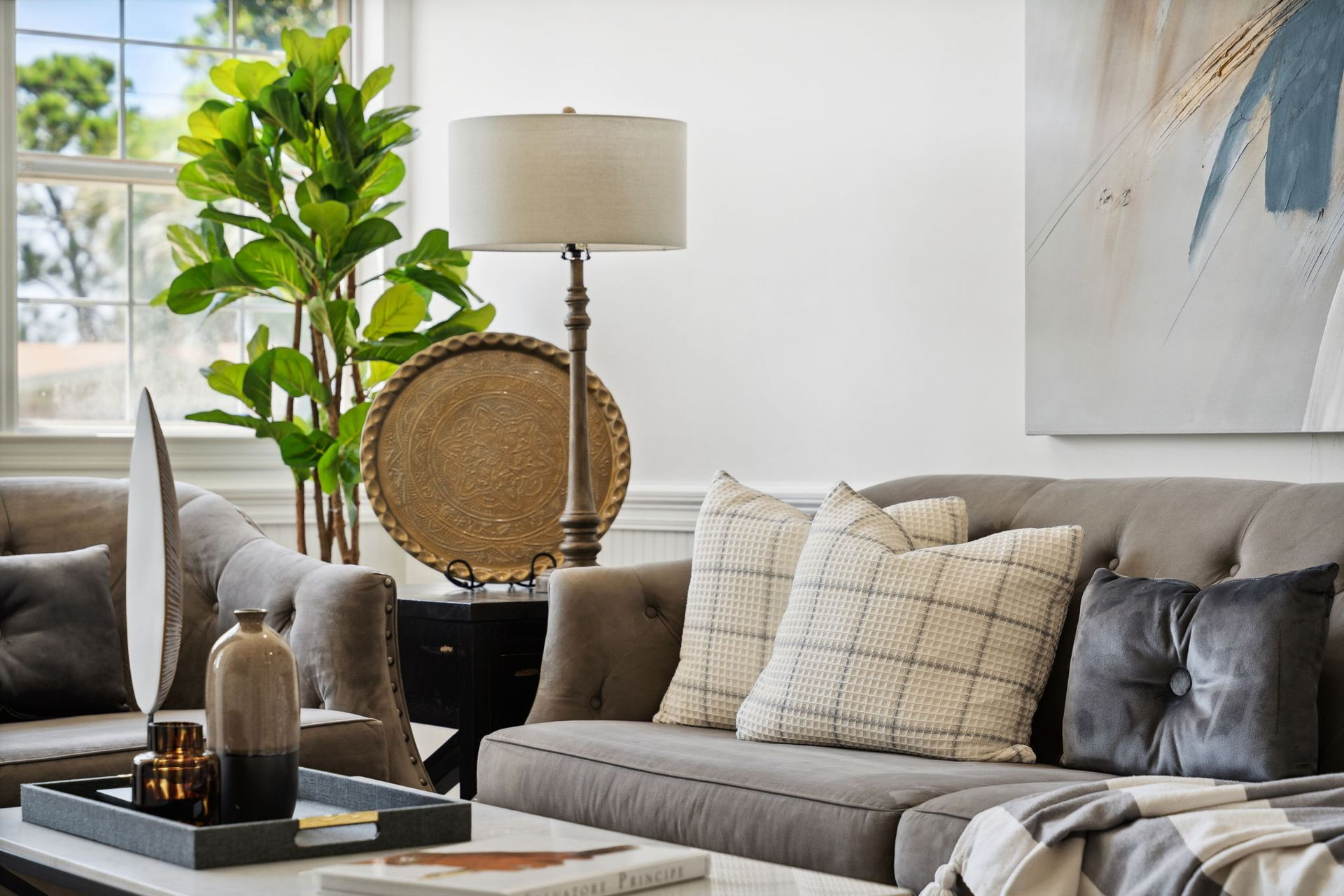 Living room with gray sofa, lamp, fiddle leaf fig, tray on coffee table, and artwork.