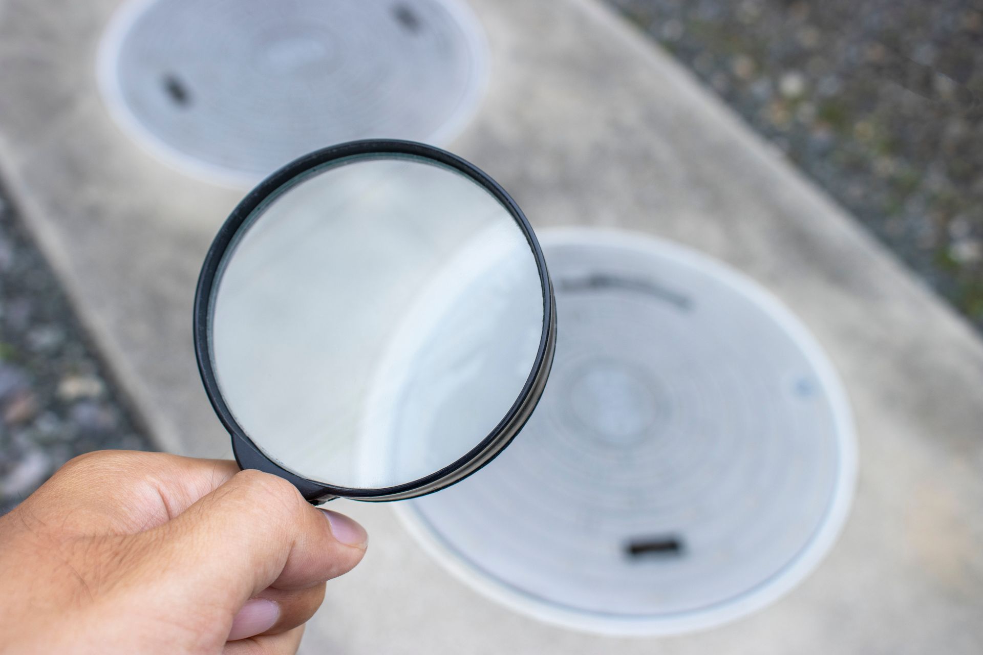 Hand holding magnifying glass over utility access covers on pavement. Hand holding magnifying glass over utility access covers on pavement.