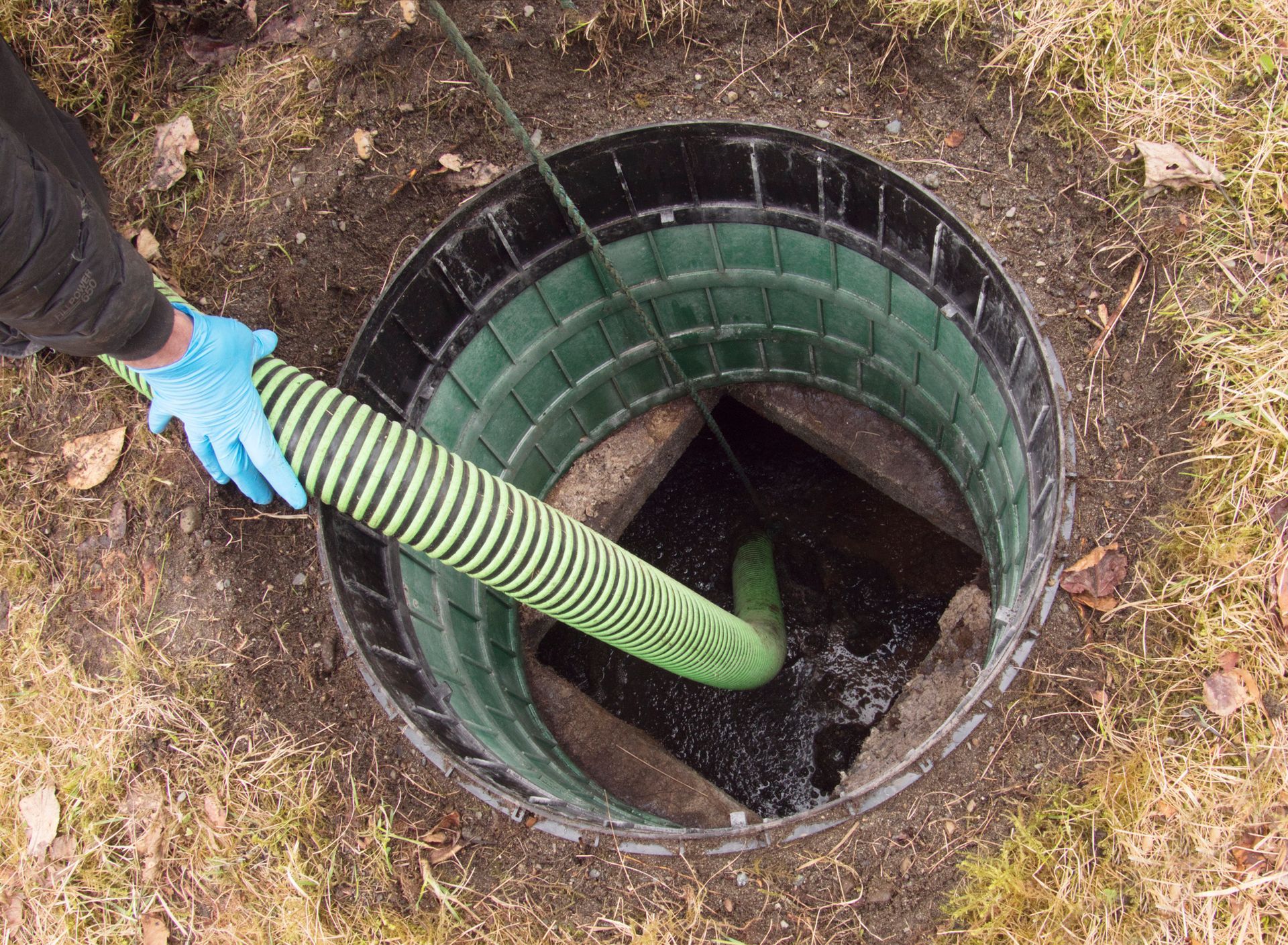 Person in blue gloves using a hose to pump liquid from a septic tank.