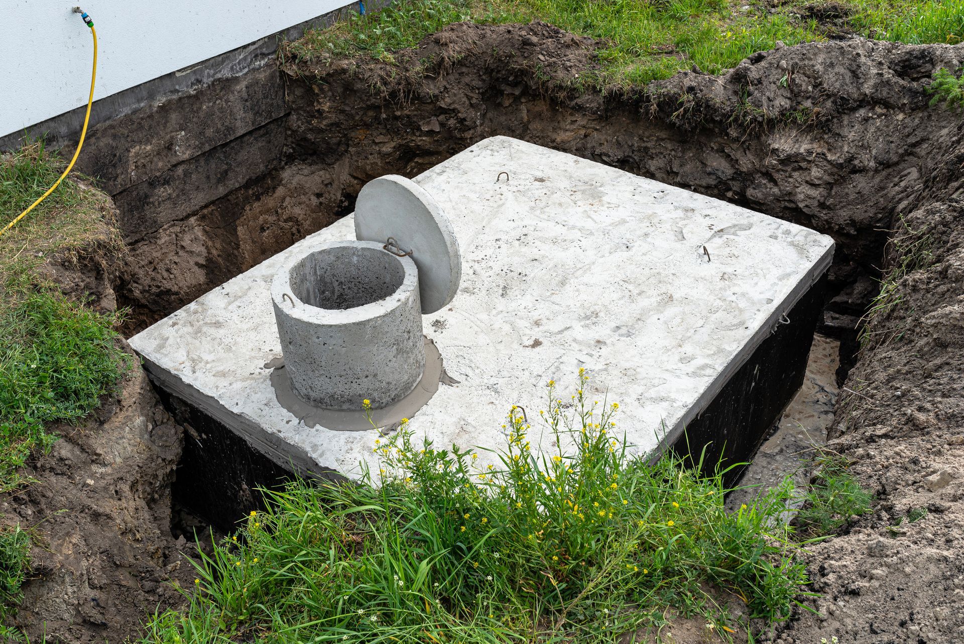 Concrete septic tank lid with an open access port, placed in a dug-out hole in the ground.