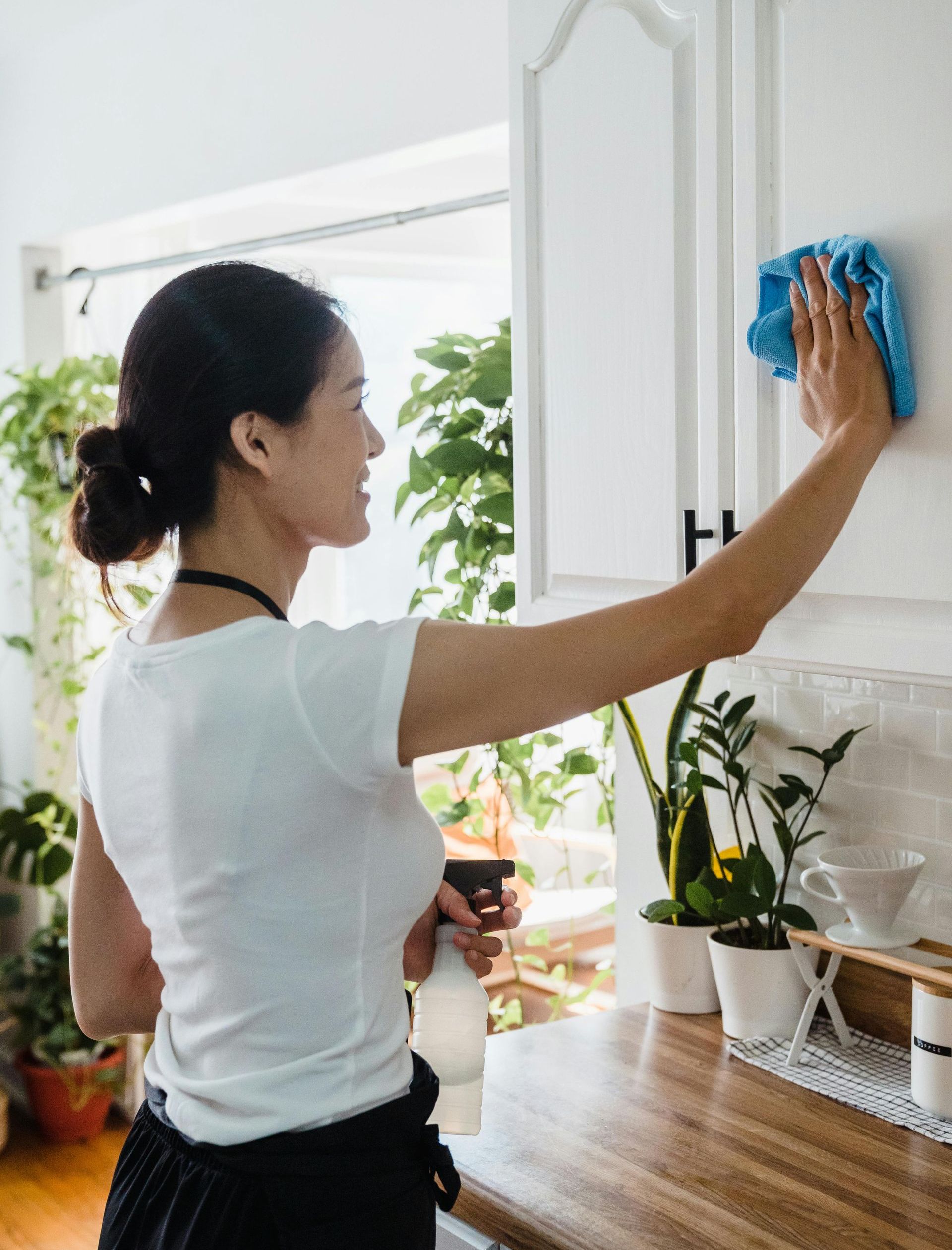 A brunette female cleaner smiling as she cleans the white kitchen cabinet displaying our airbnb cleaning service in chicago