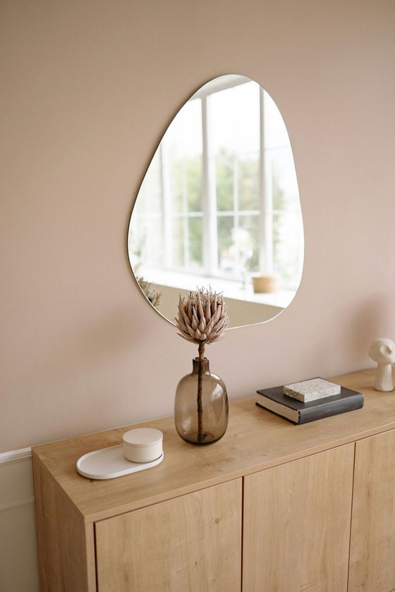 A large mirror is hanging on a wall above a wooden dresser.