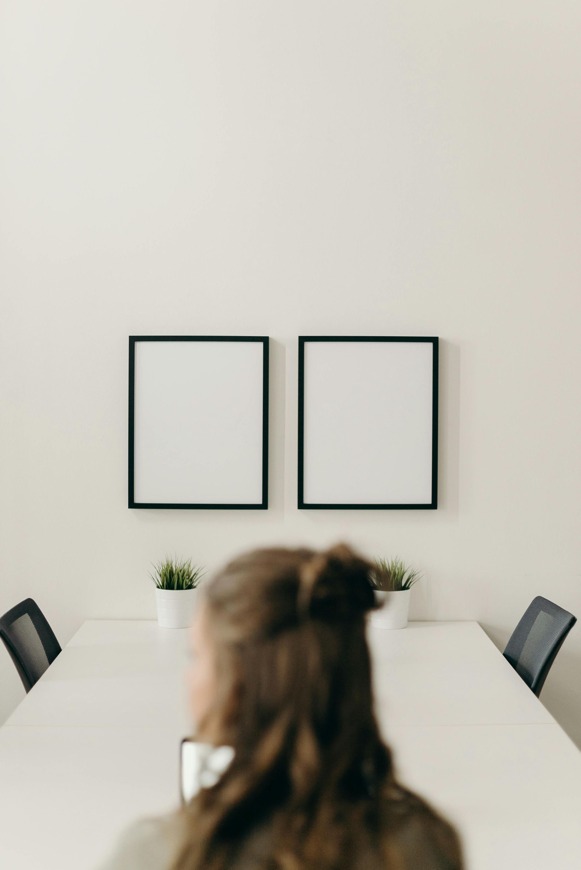 A woman is sitting at a table in a conference room with two empty frames on the wall.