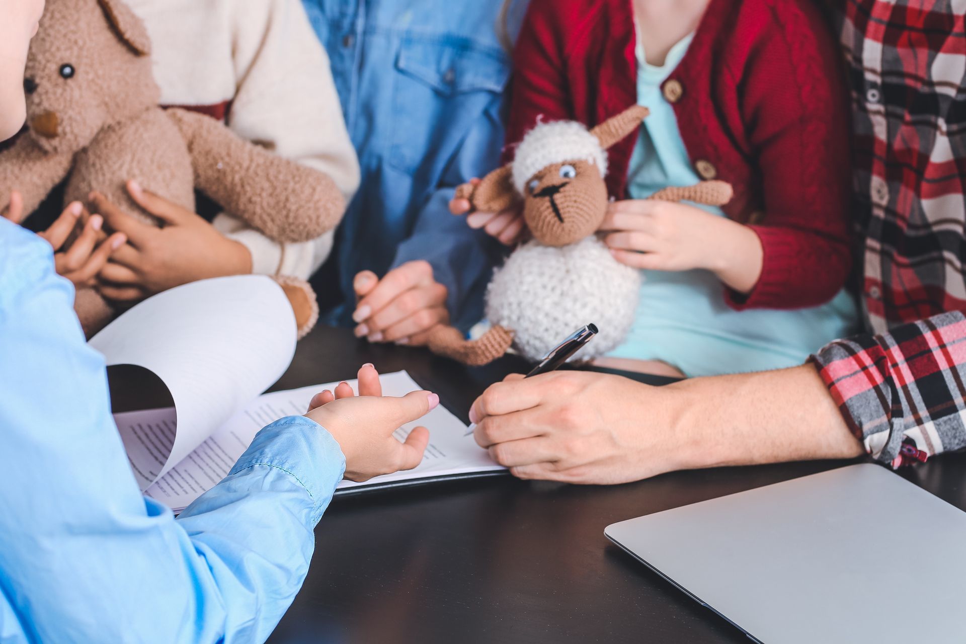 A cropped view of a lawyer meeting with two clients holding children signing documents.