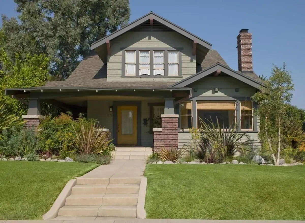Craftsman-style house with front lawn, brick chimney, and walkway on a sunny day