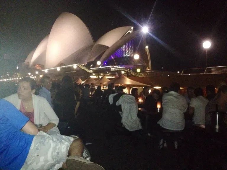 A group of people sitting in front of the opera house at night
