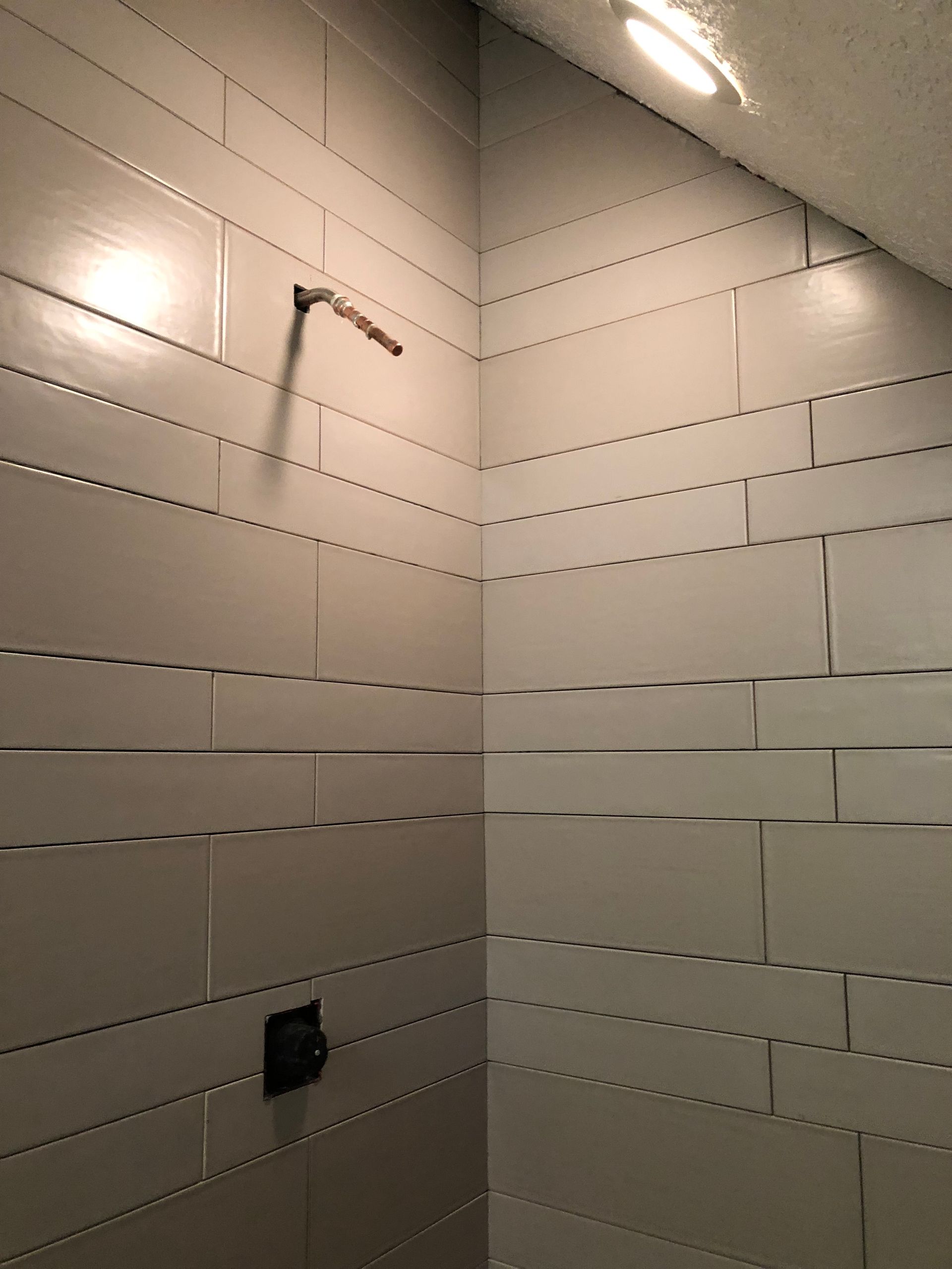 A shower with white tiles and a black shower head.