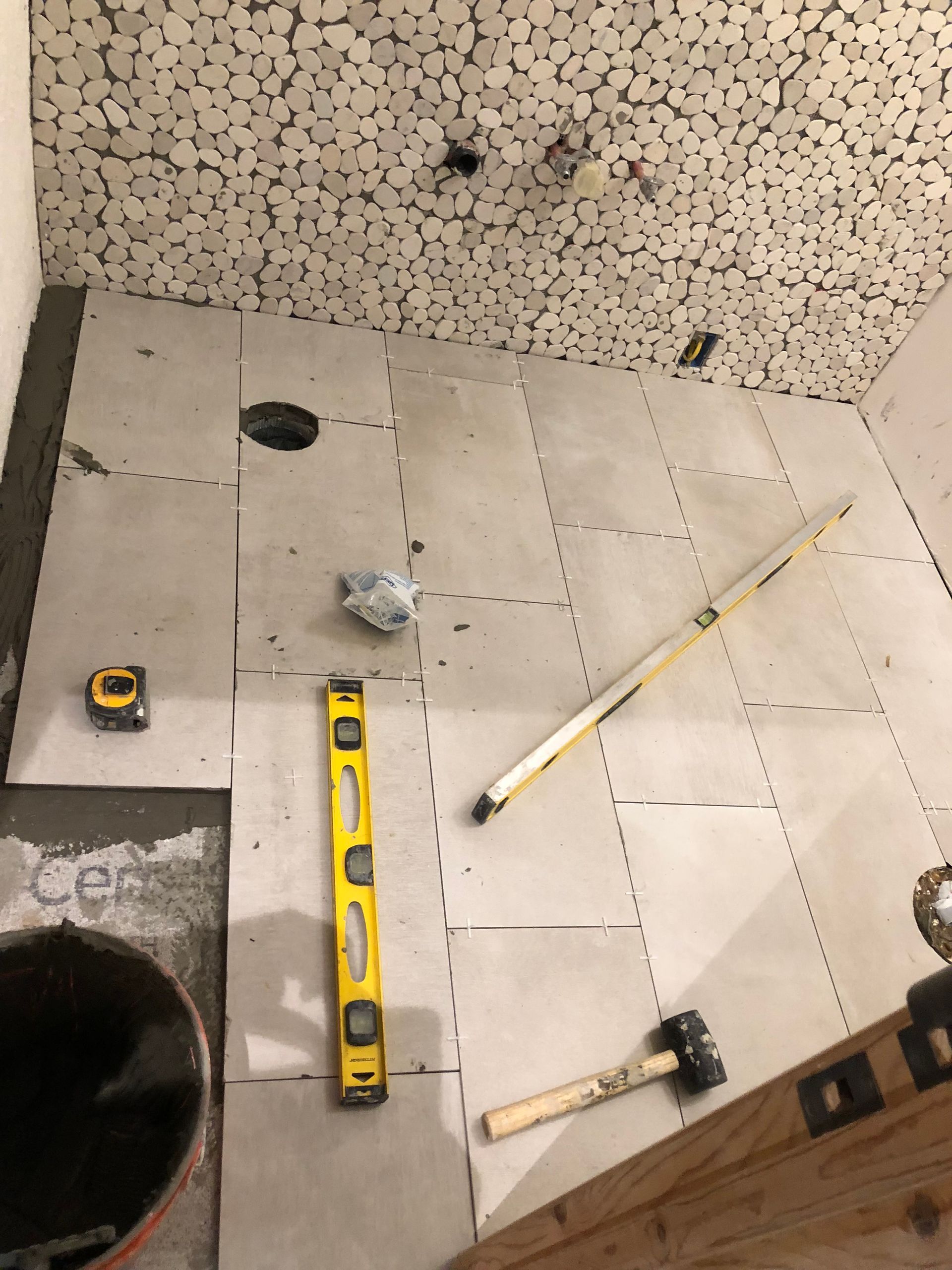 A yellow level is sitting on a tiled floor next to a hammer and tape measure.