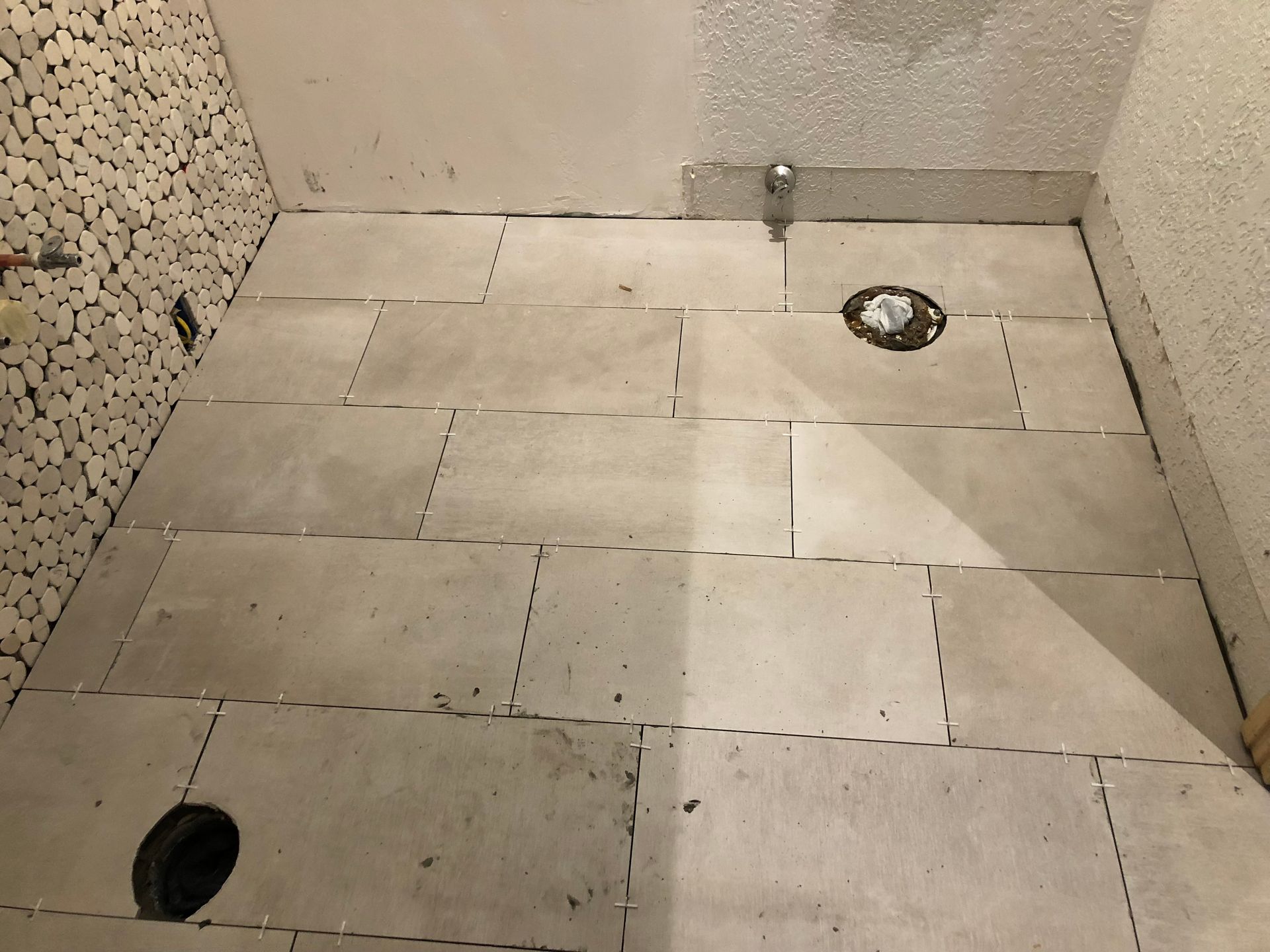 A bathroom floor with white tiles and a hole in the middle