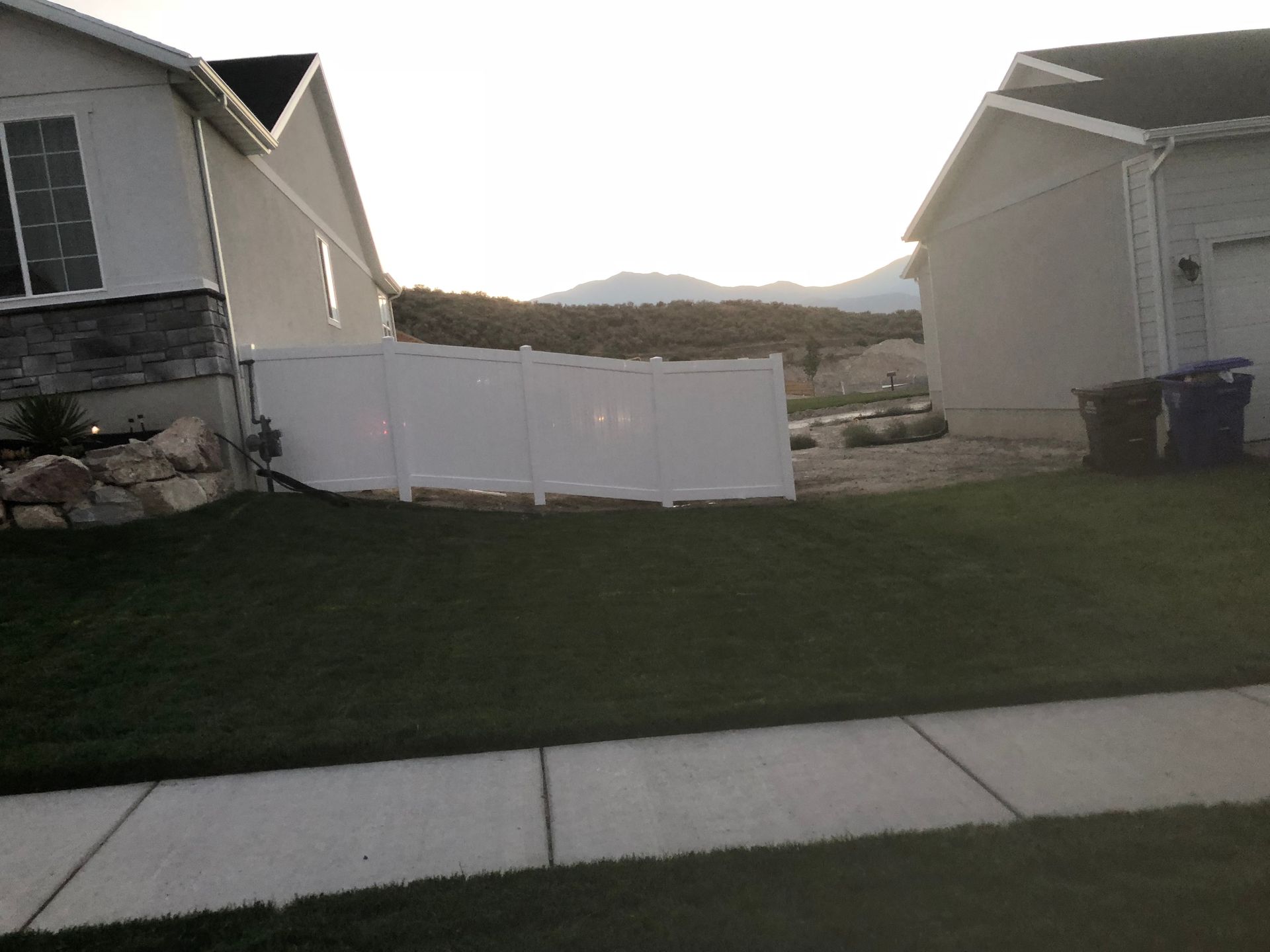 A white fence surrounds a lush green lawn in front of a house.