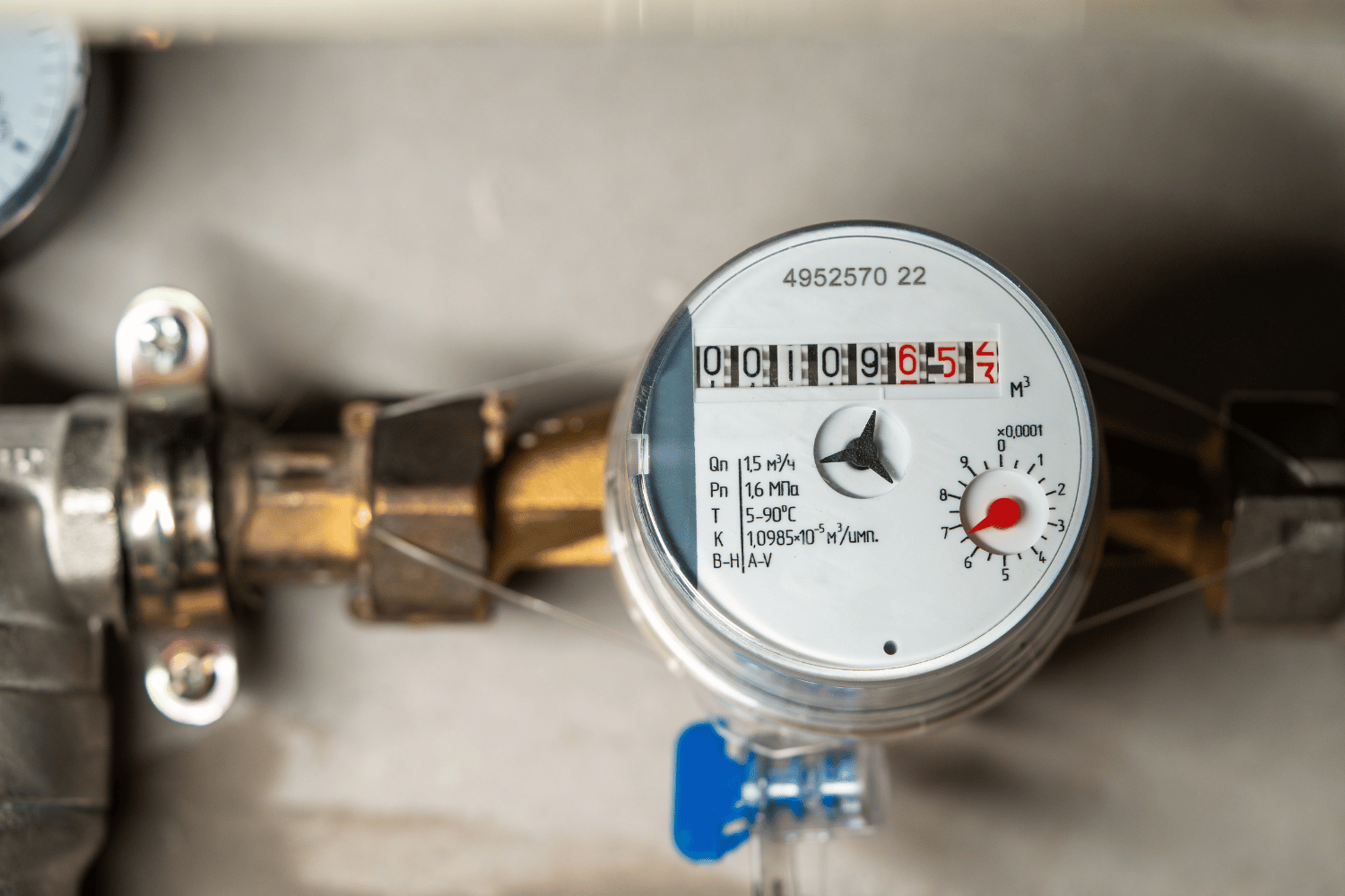 Close-up of a gas meter with pipes and a blue valve attached to a wall