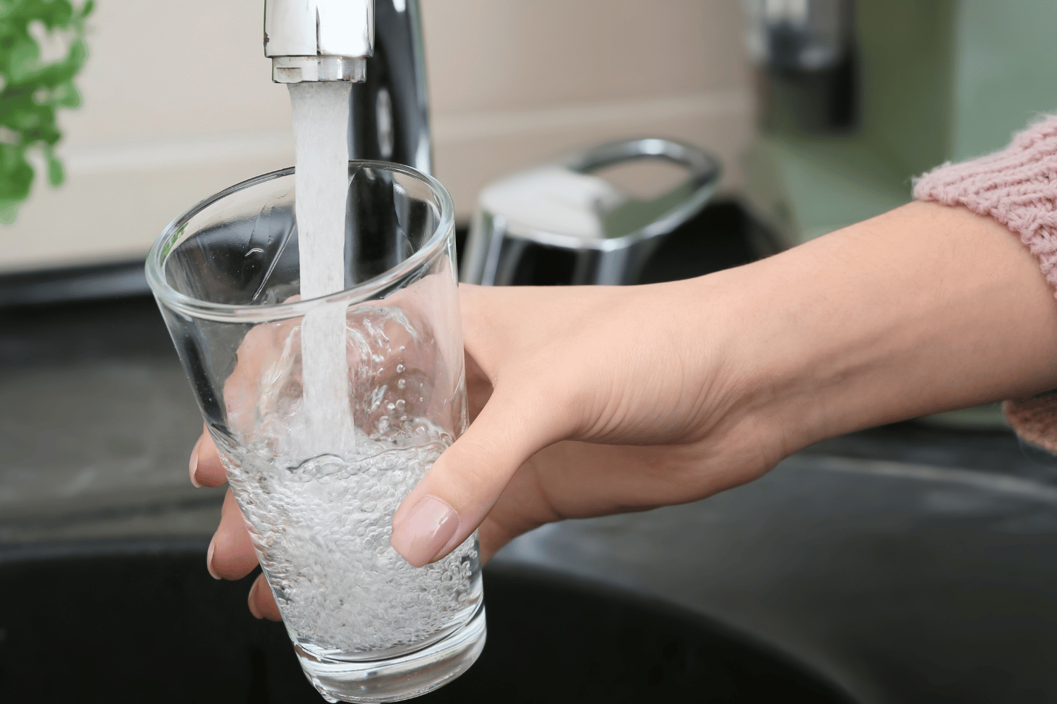 Hand filling a clear glass with running water at a kitchen sink