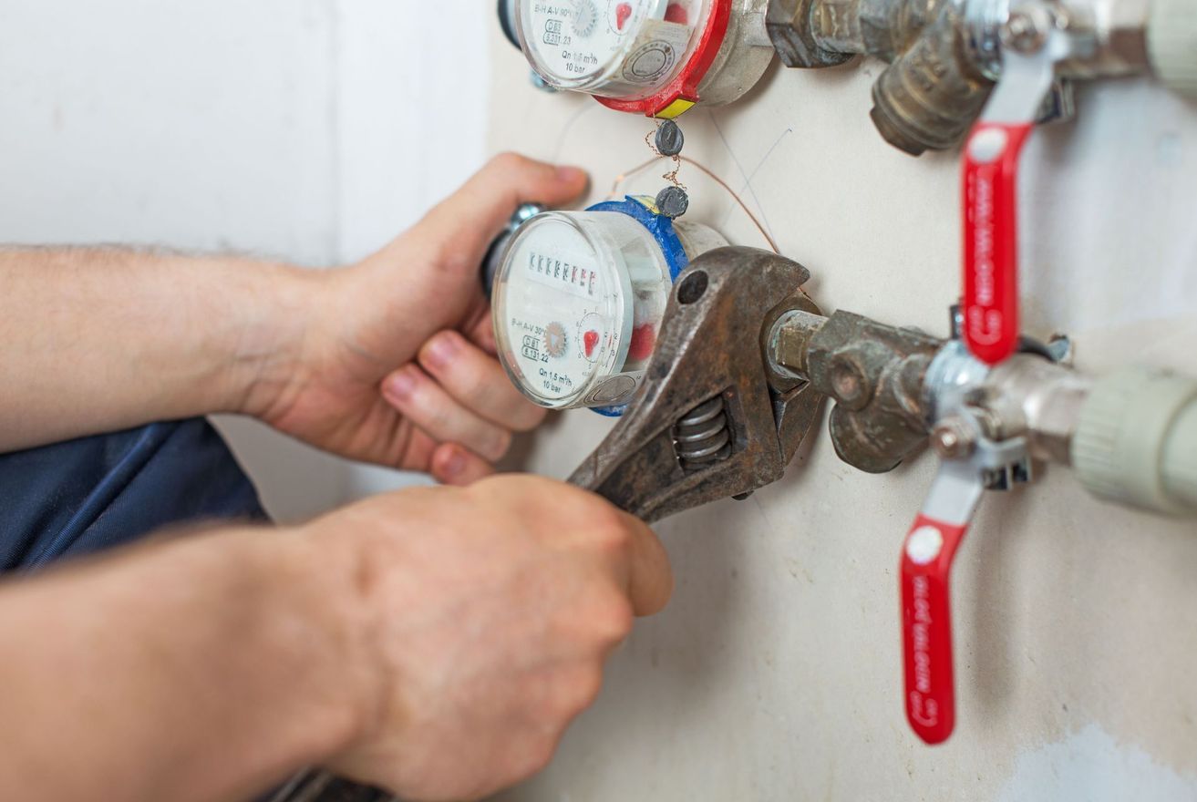 Hand adjusting a water meter valve with a wrench beside red shutoff valves