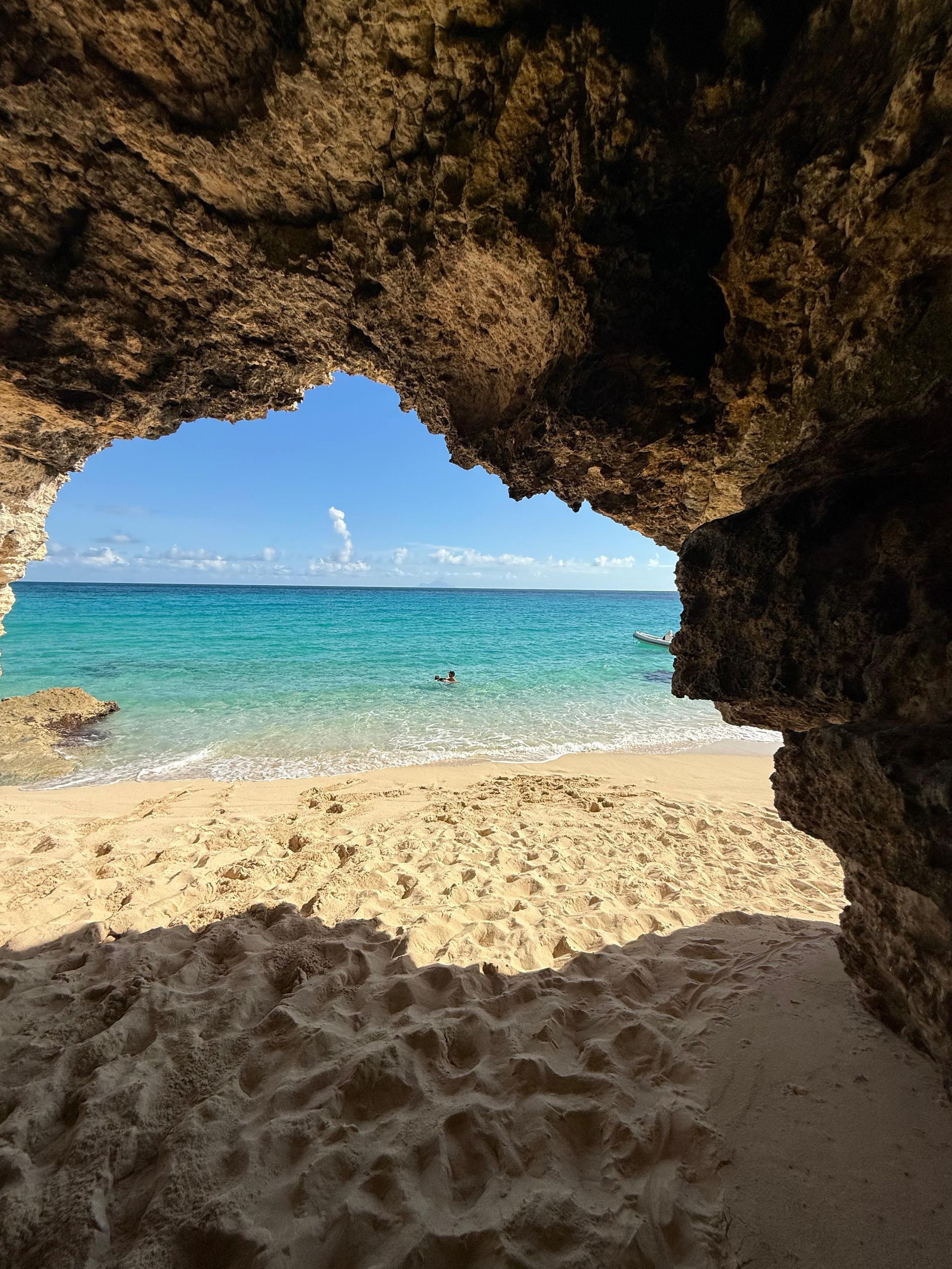 Cave opening frames a view of a tropical beach with turquoise water and blue sky.