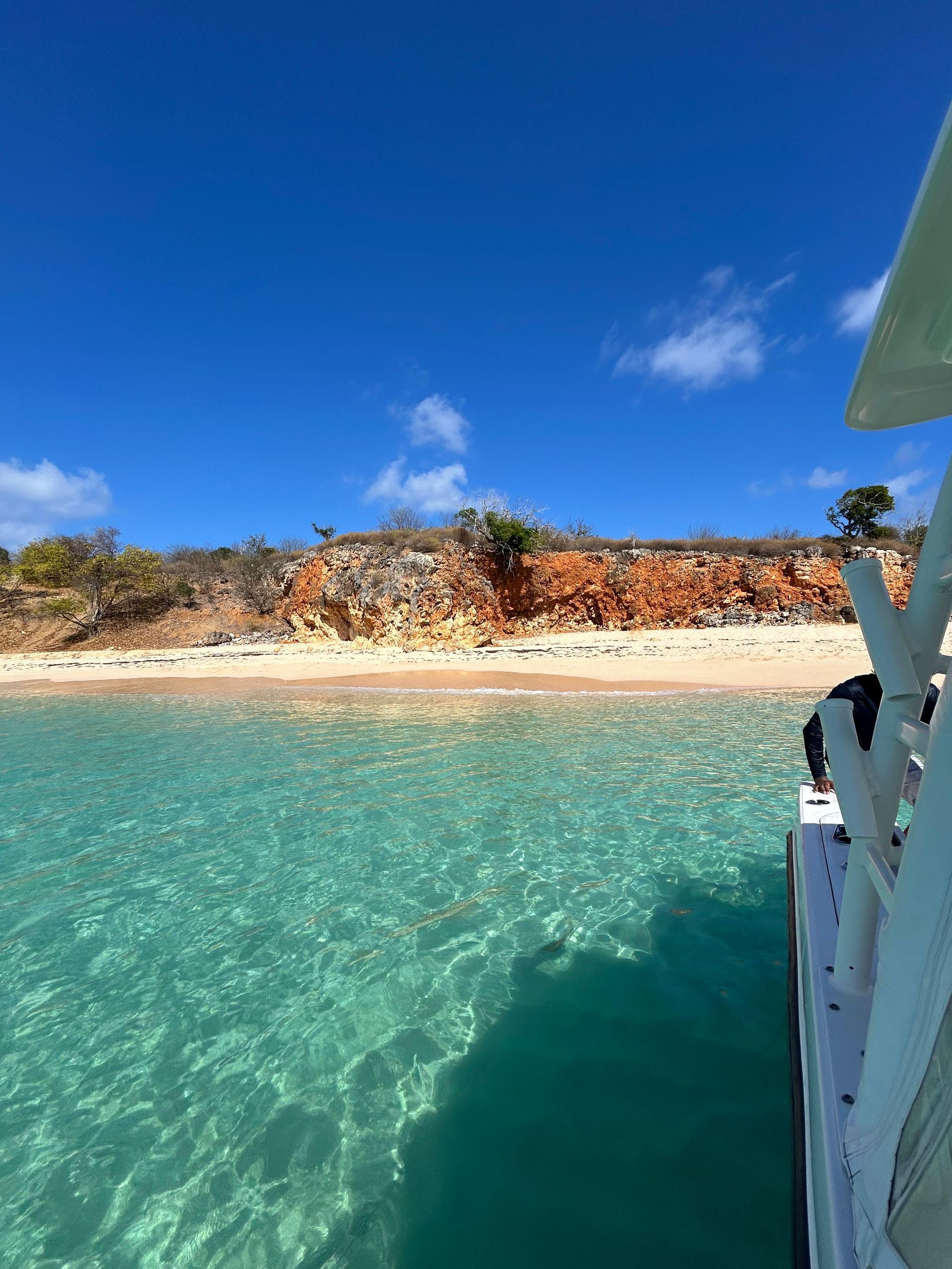 Boat on clear turquoise water near a red-cliffed shore under a bright blue sky.