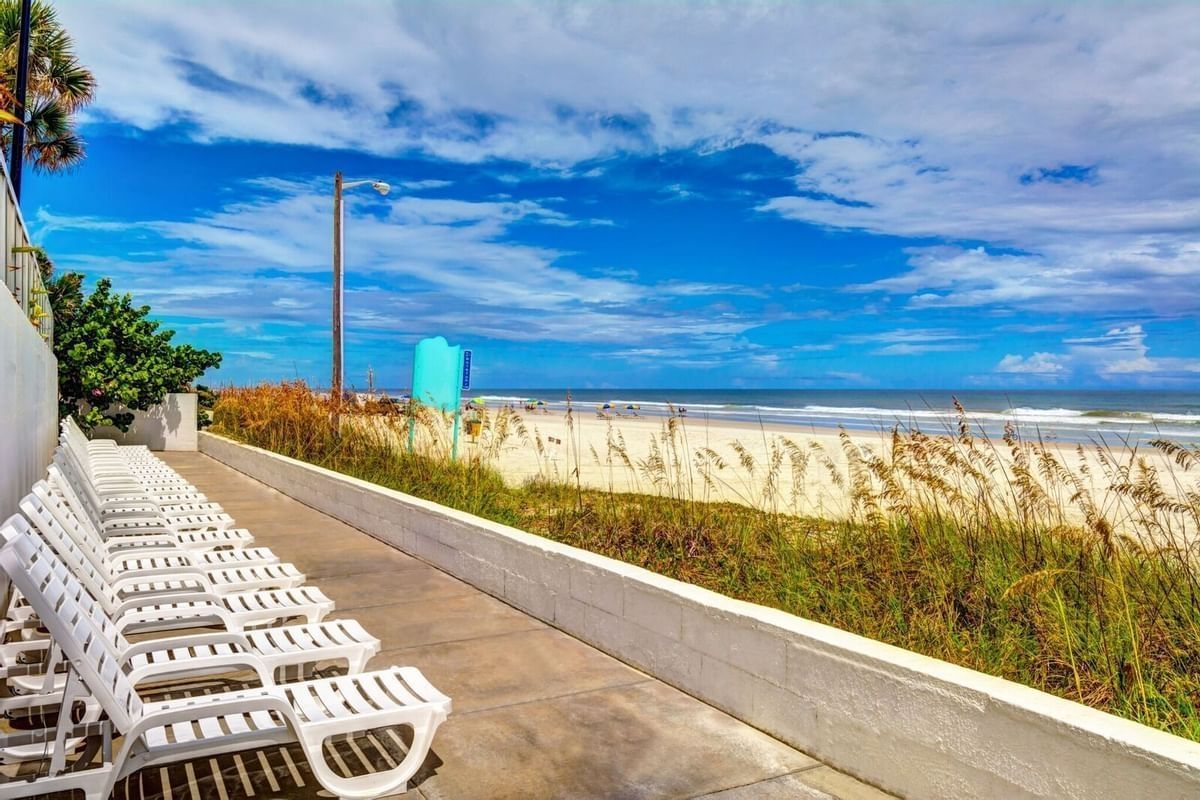 Lounge chairs on a walkway overlook a beach with blue sky and white clouds.