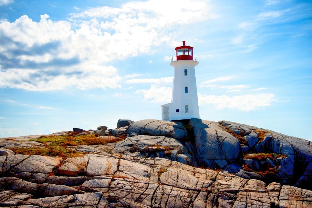 White lighthouse on a rocky outcropping, under a blue sky with fluffy clouds.