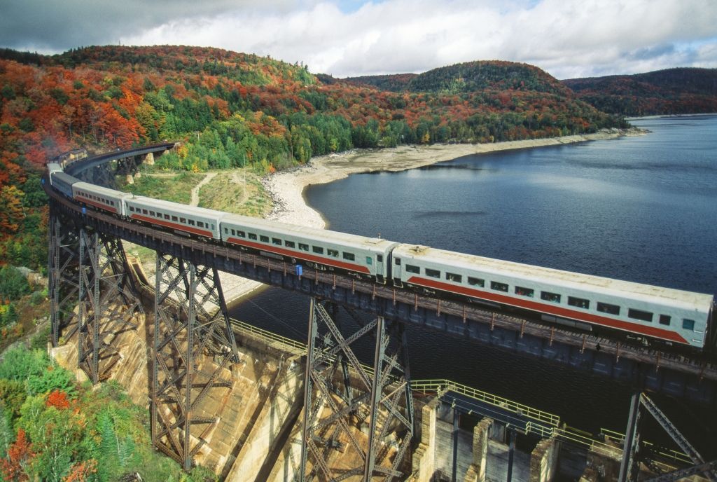 Train crossing a tall bridge over water, fall foliage in the background.