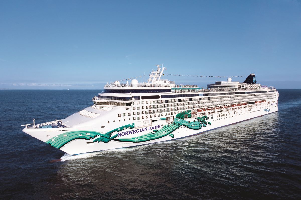 A large white cruise ship, painted with a green dragon, sailing on blue water under a clear sky.