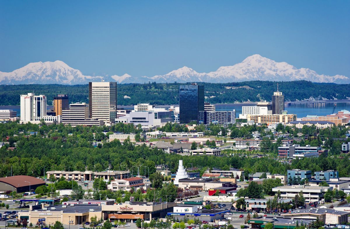 Anchorage, Alaska skyline with mountains, trees, and buildings under a blue sky.